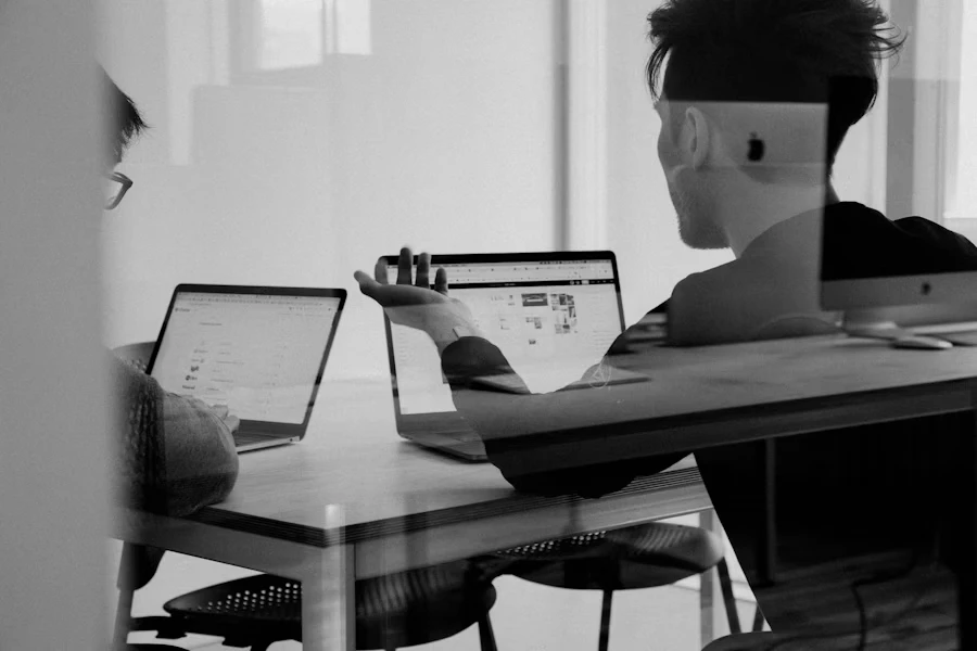 Two colleagues comparing work on laptops at a shared desk